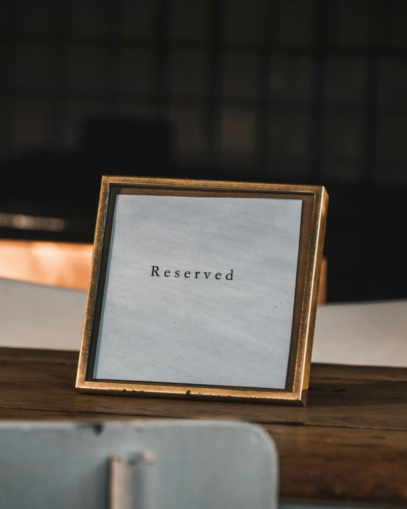 A small framed 'Reserved' card on a dark wooden restaurant table with empty chairs behind.