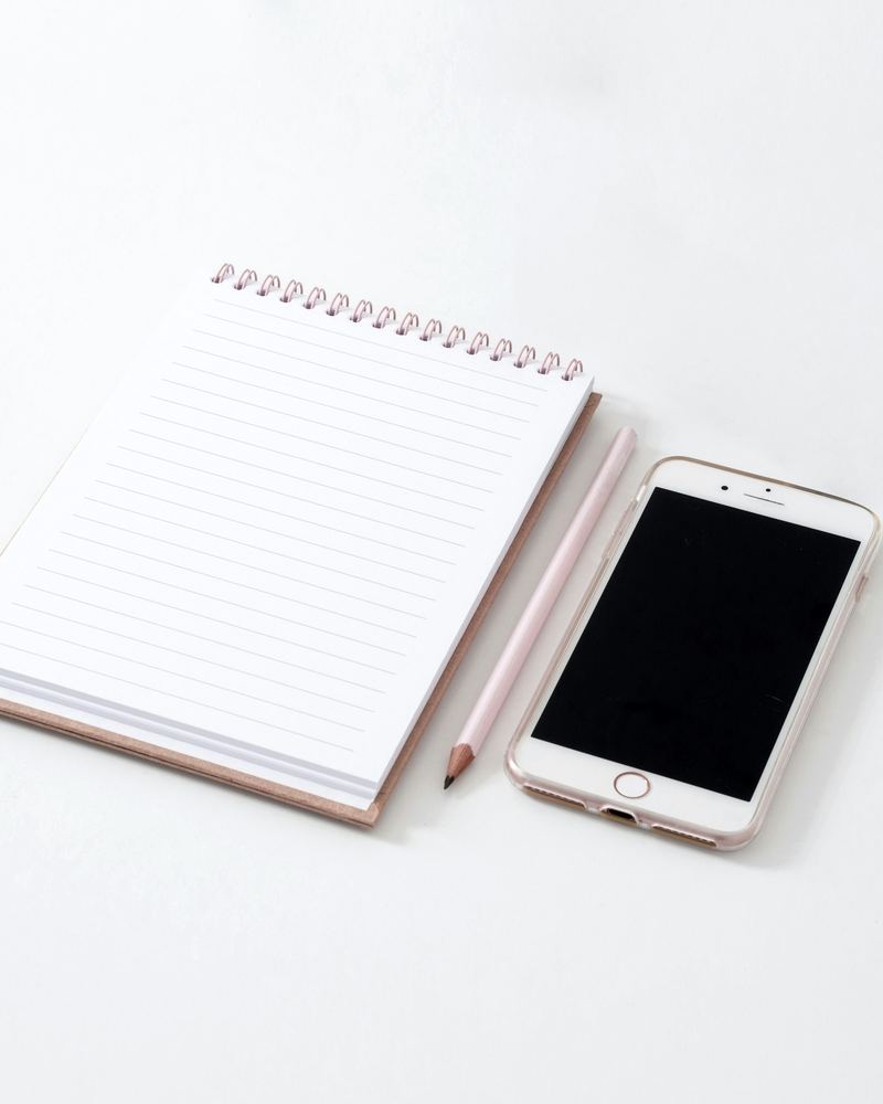 A phone with a dark screen lying beside a lined notepad and a pencil.