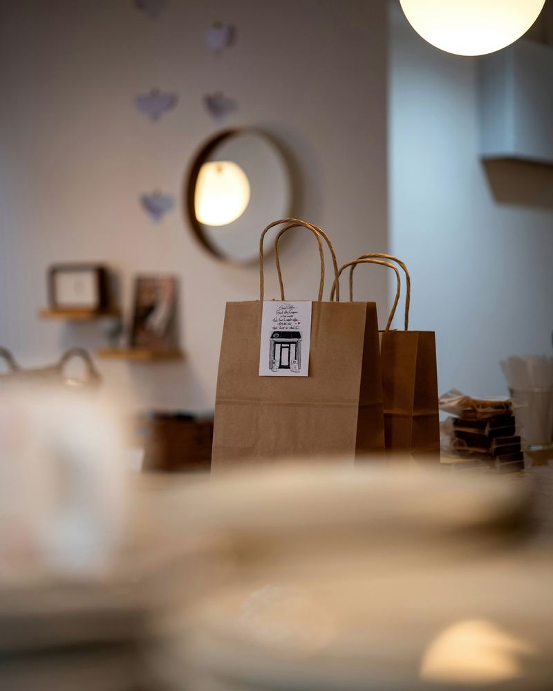 Two plain paper carrier bags waiting on a café counter, with plates blurred in the foreground.