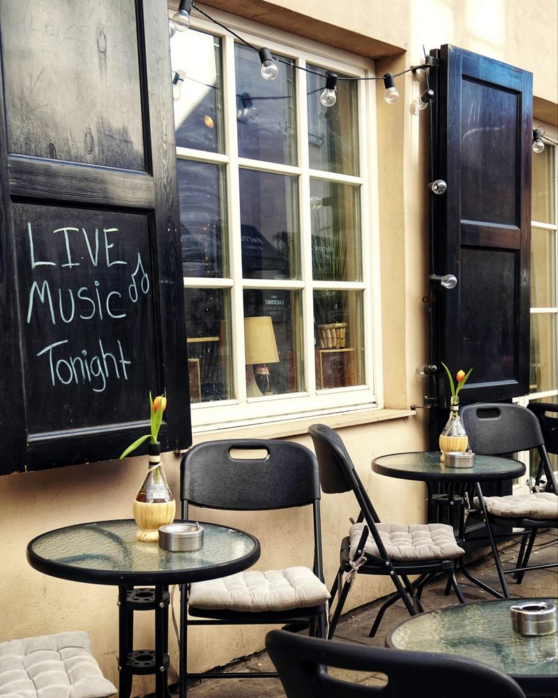 A chalkboard on a café shutter reading 'Live music tonight' above small outdoor tables.