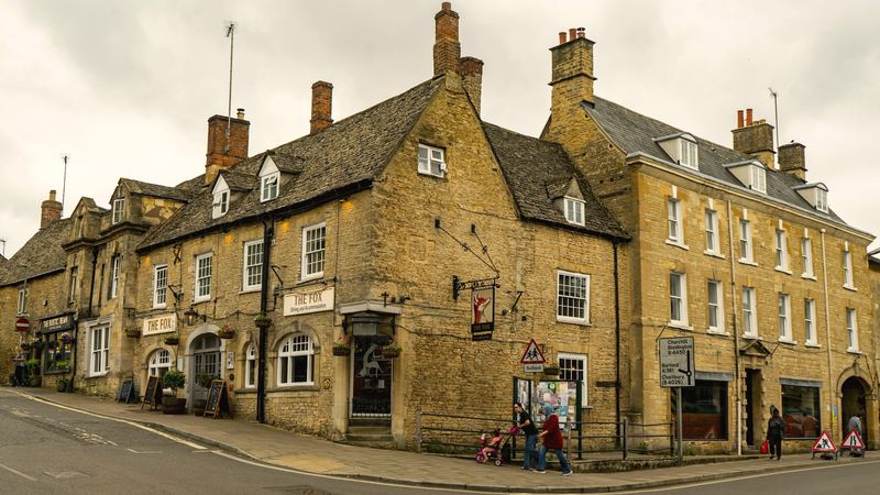 A honey-coloured stone building on a corner in a small town under a soft grey sky.