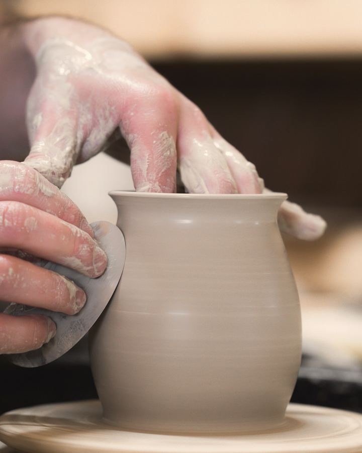 A potter's hands shaping a clay pot on the wheel.