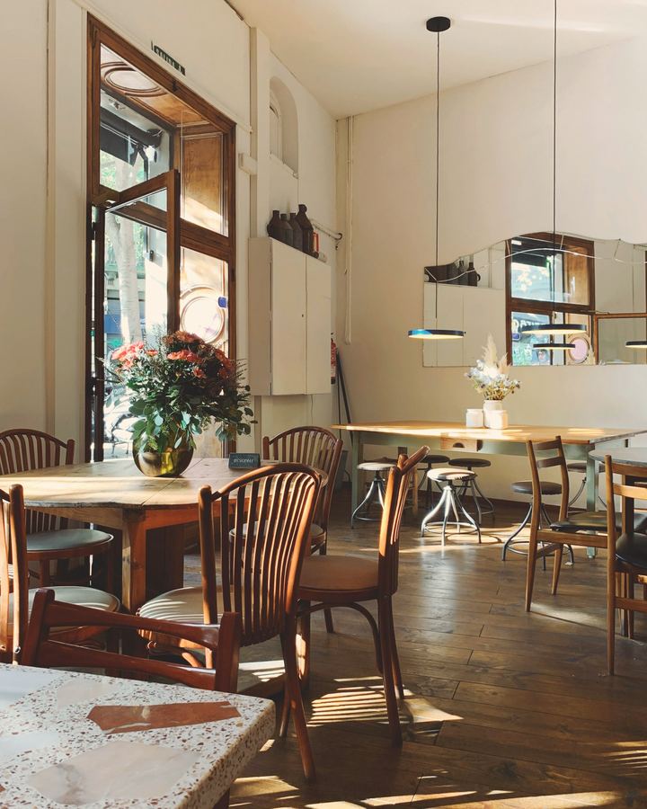 A bright café interior with wooden tables and chairs in window light, before anyone arrives.