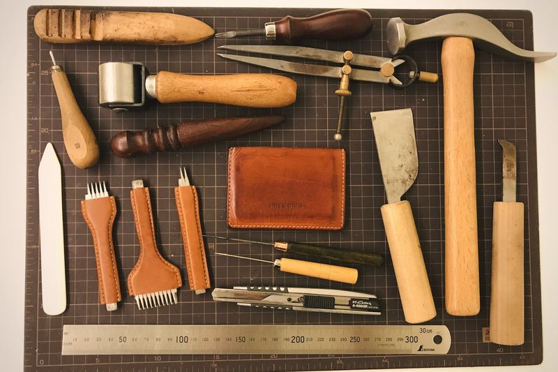 Leatherworking tools laid out on a cutting mat beside a small leather wallet.